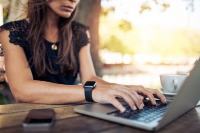 44972543 - young woman wearing smartwatch using laptop computer. female working on laptop in an outdoor cafe.